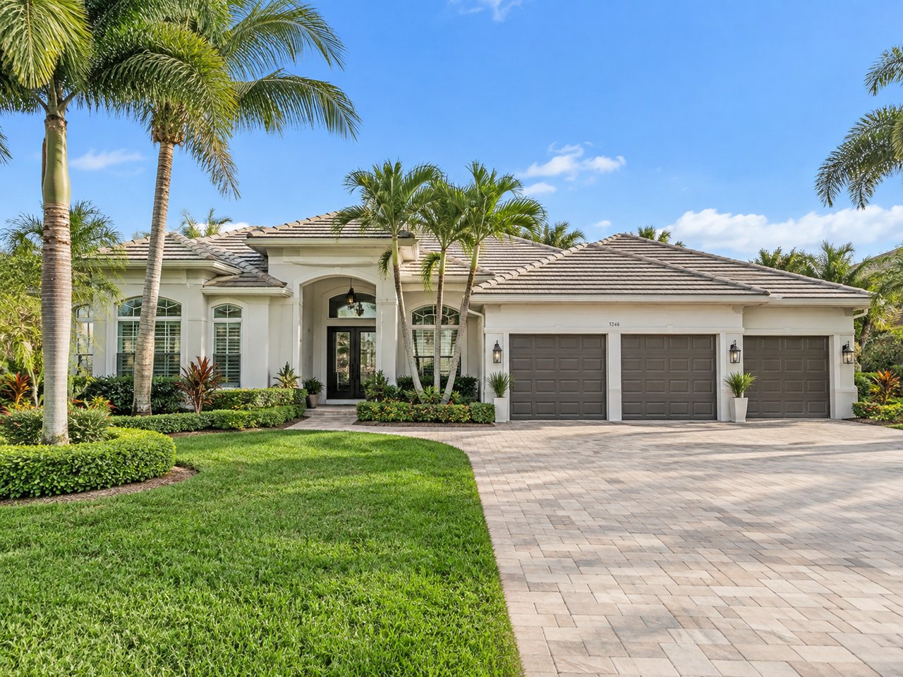 White single-story home with a three-car garage, palm trees, and a broad paved driveway.