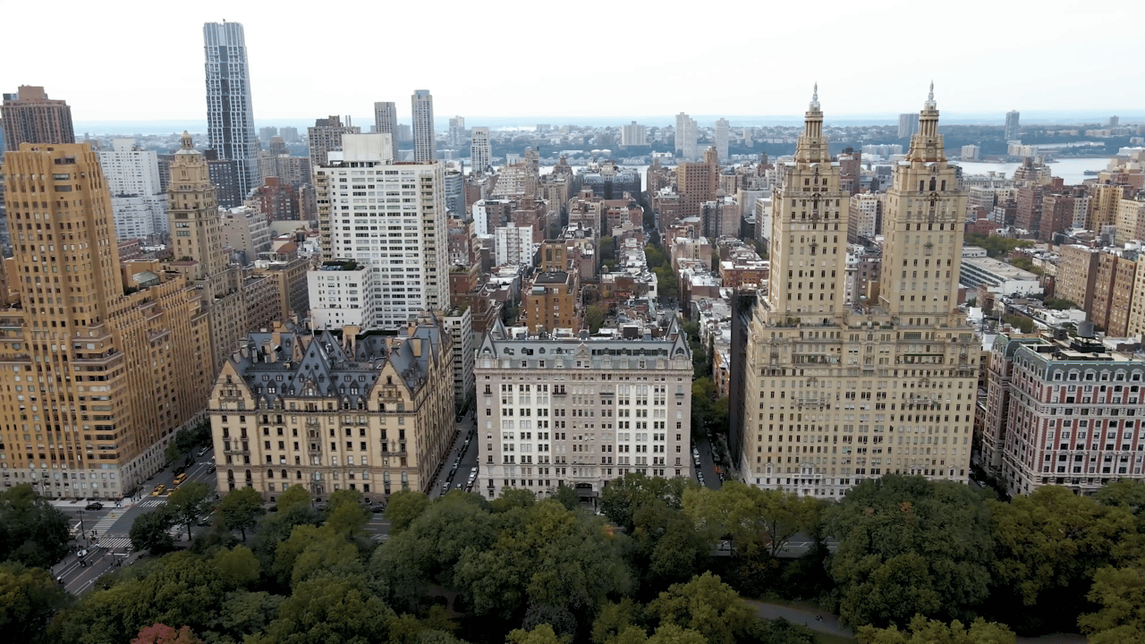 Aerial panorama of New York City buildings, with a leafy park in the foreground and twin towers on the right.