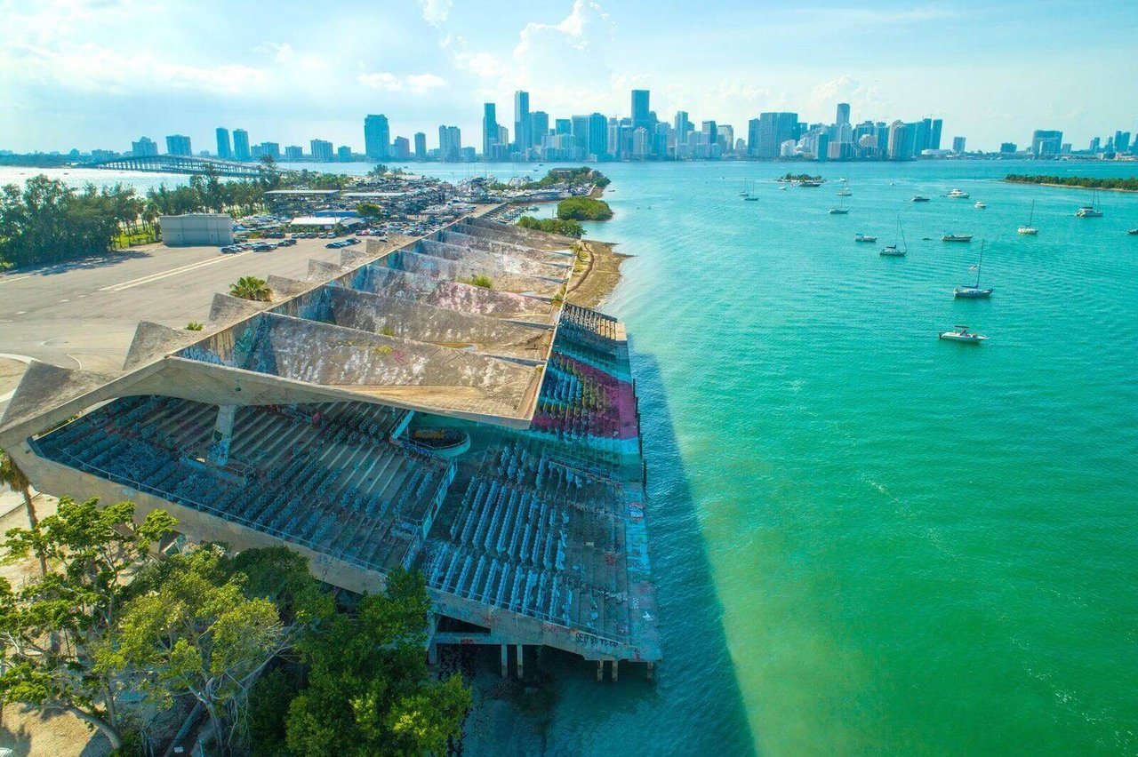 Aerial view of the Miami Marine Stadium and its unique cantilevered roof, over turquoise waters looking towards downtown Miami.
