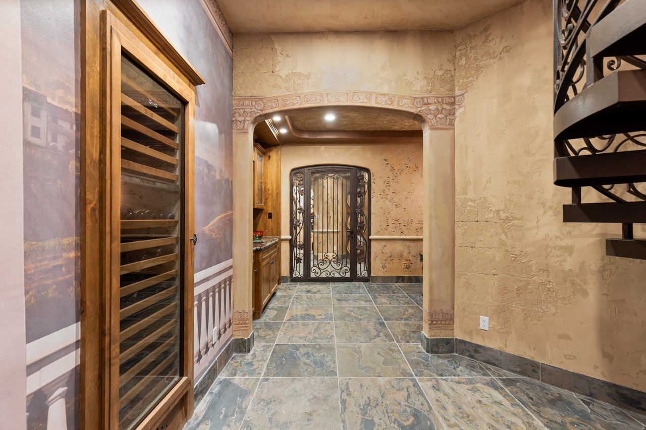 Wine cellar with a glass-fronted wooden wine rack, ornate archway, and wrought-iron gate.