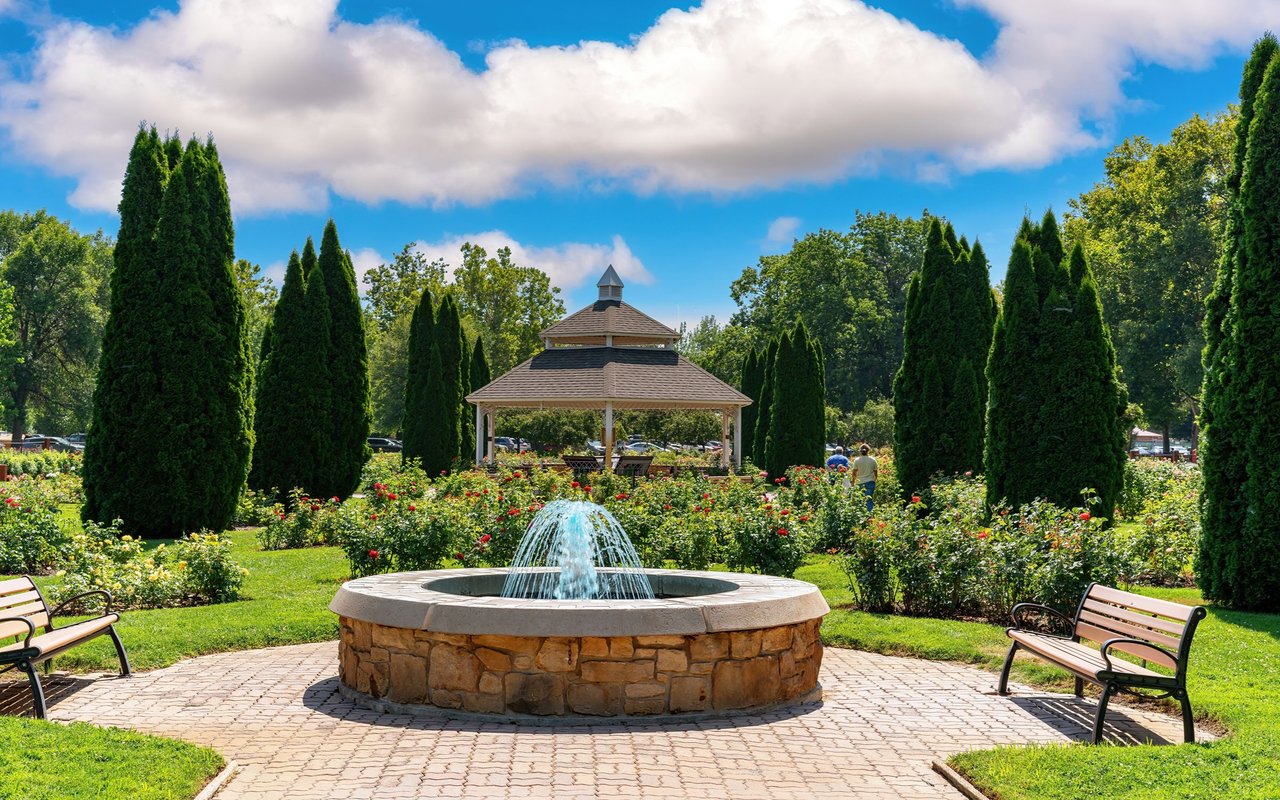 Garden fountain with rose beds, evergreen trees, benches, and a gazebo.