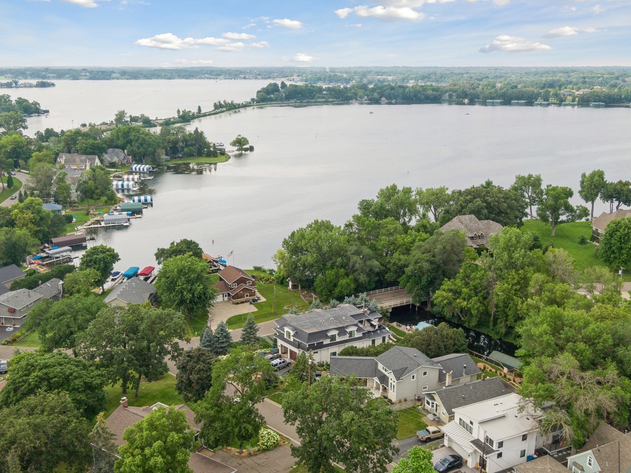 An aerial view of luxury residential homes with private boat docks lining a tranquil bay near Lake Minnetonka, showcasing prime West Metro real estate.