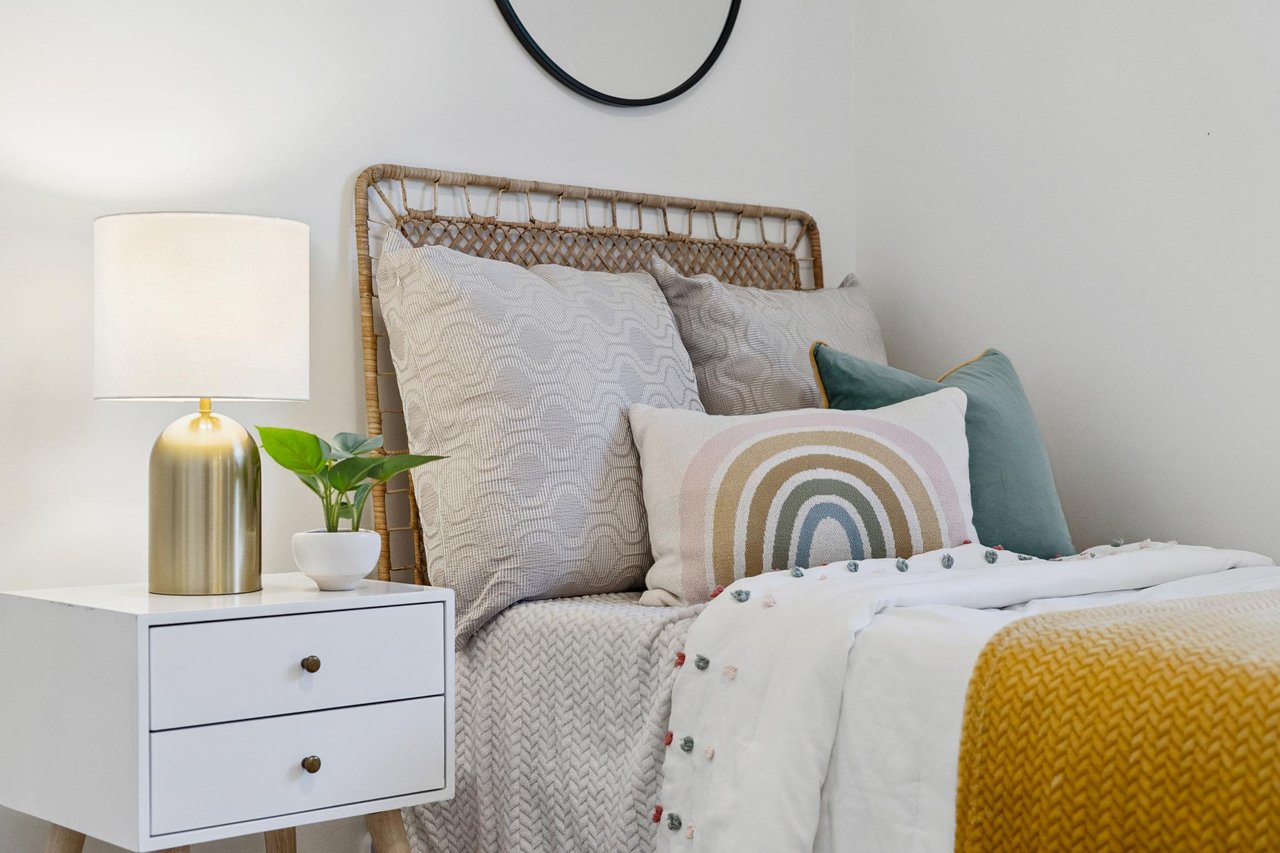 Staged bedroom with a woven headboard, layered pillows, and a mustard yellow throw.