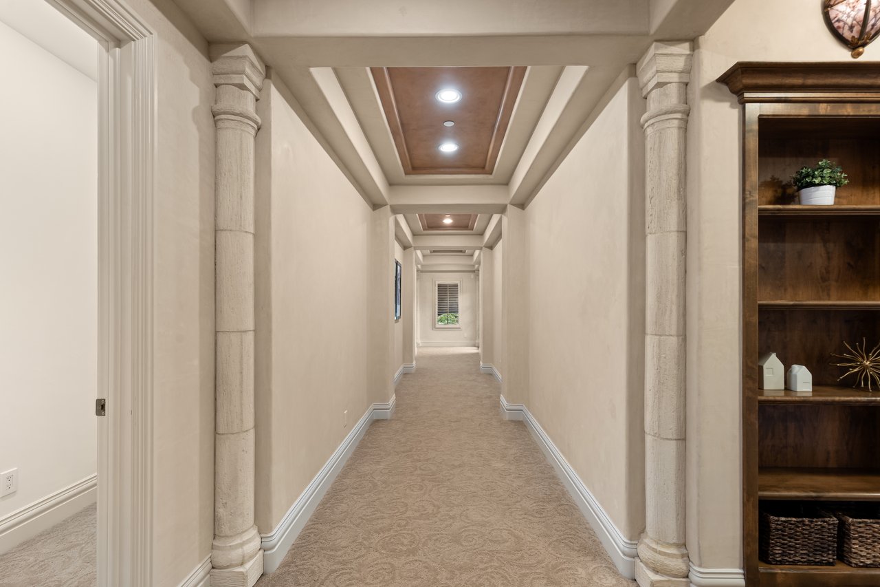 Carpeted hallway with decorative stone columns, a coffered ceiling, and built-in wooden shelving.