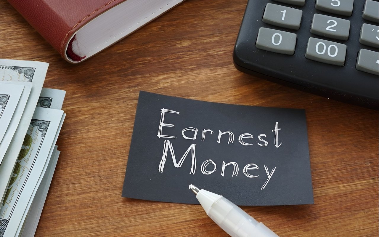 Earnest Money card beside a calculator, cash, and marker on a wooden desk.