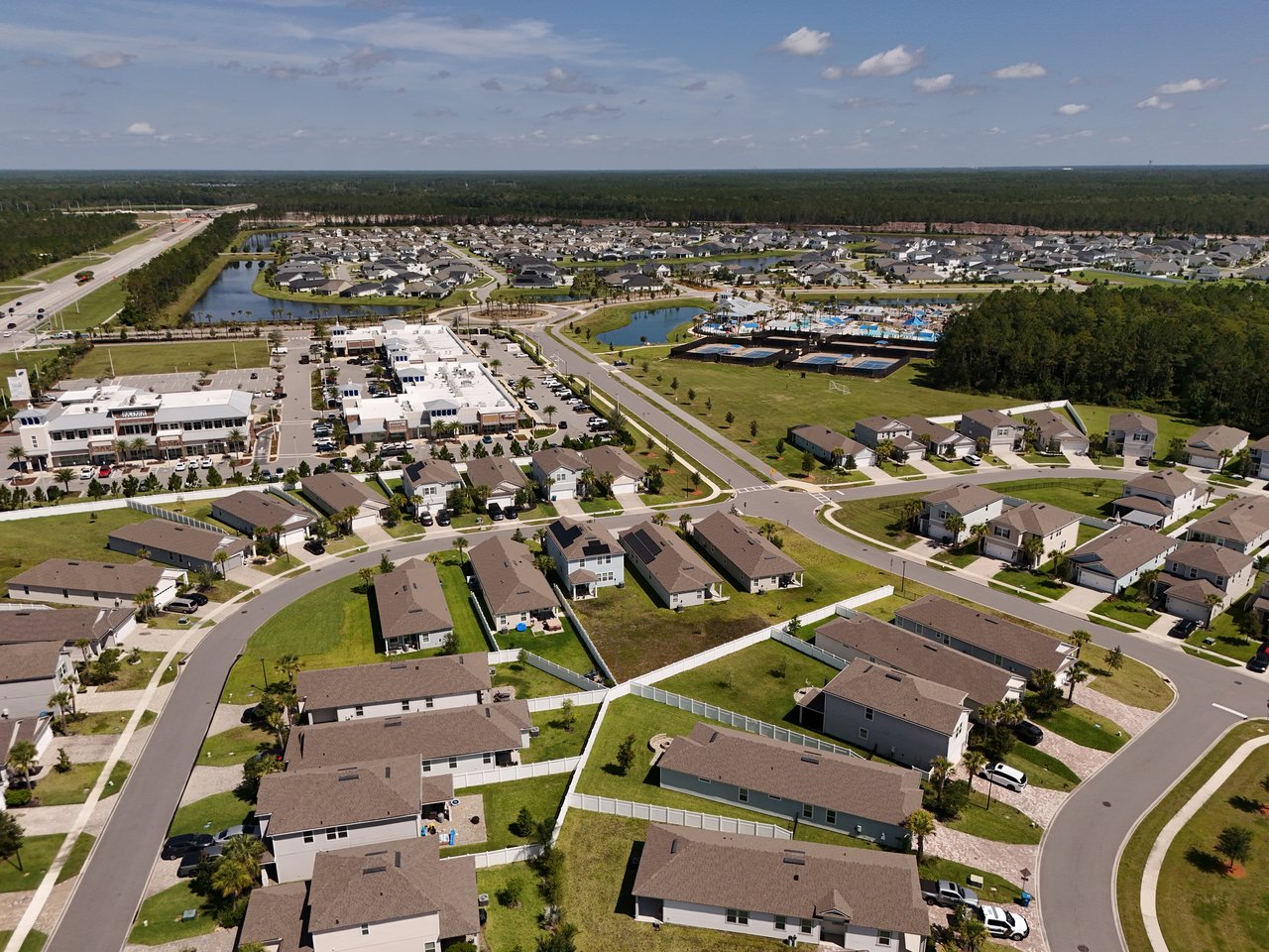 Aerial view of a residential community with ponds, a pool complex, shops, and nearby highway.