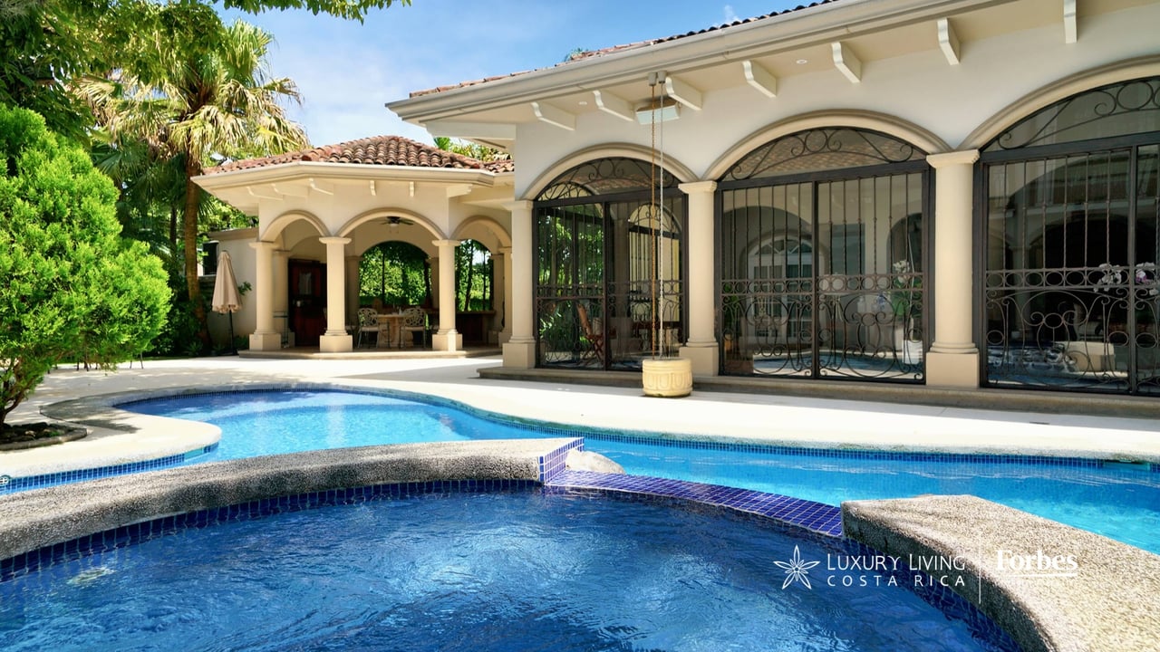 Cream-colored home with arched windows behind a curved swimming pool and covered patio.