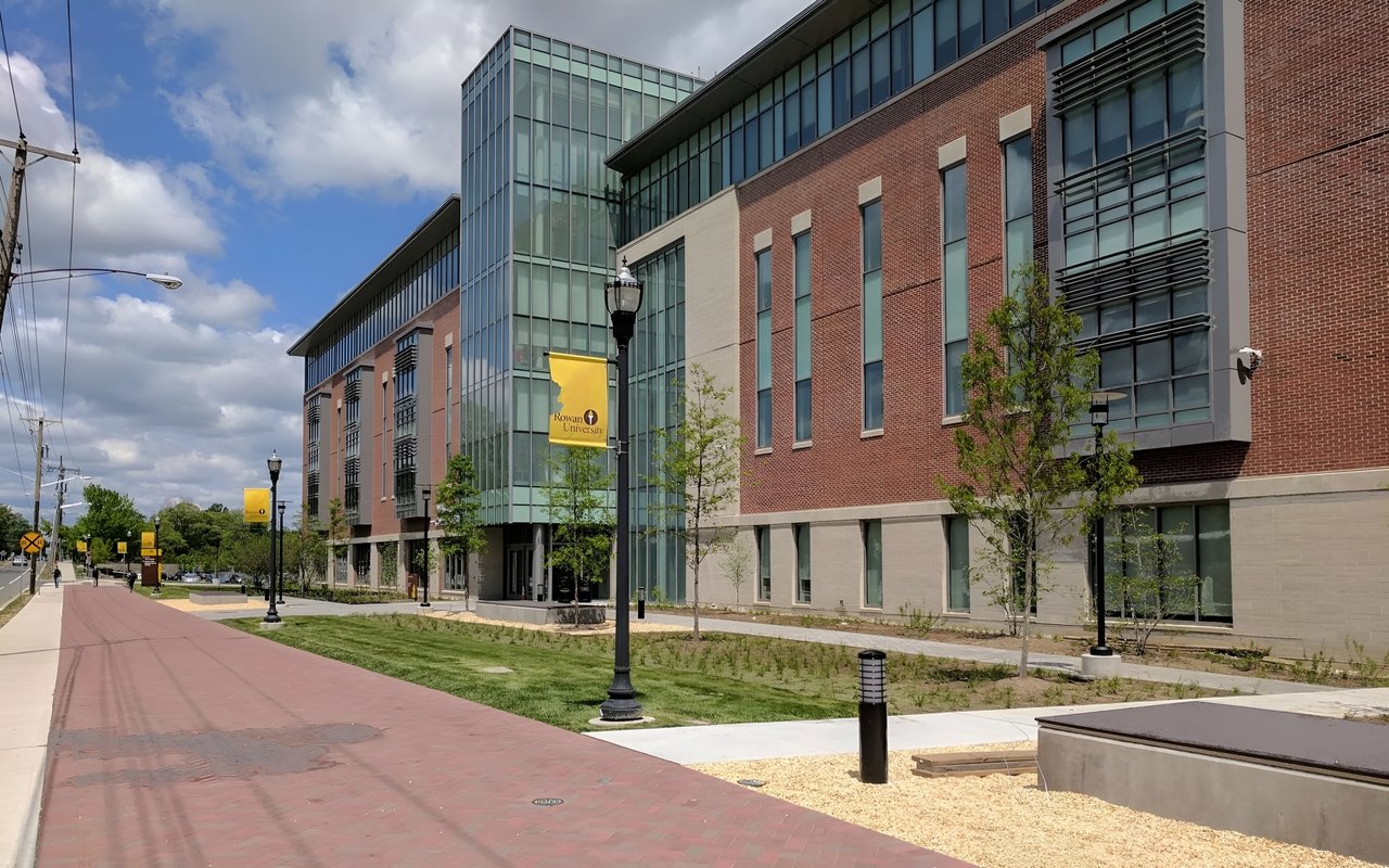 Rowan University campus building with brick and glass facades beside a landscaped pedestrian walkway.