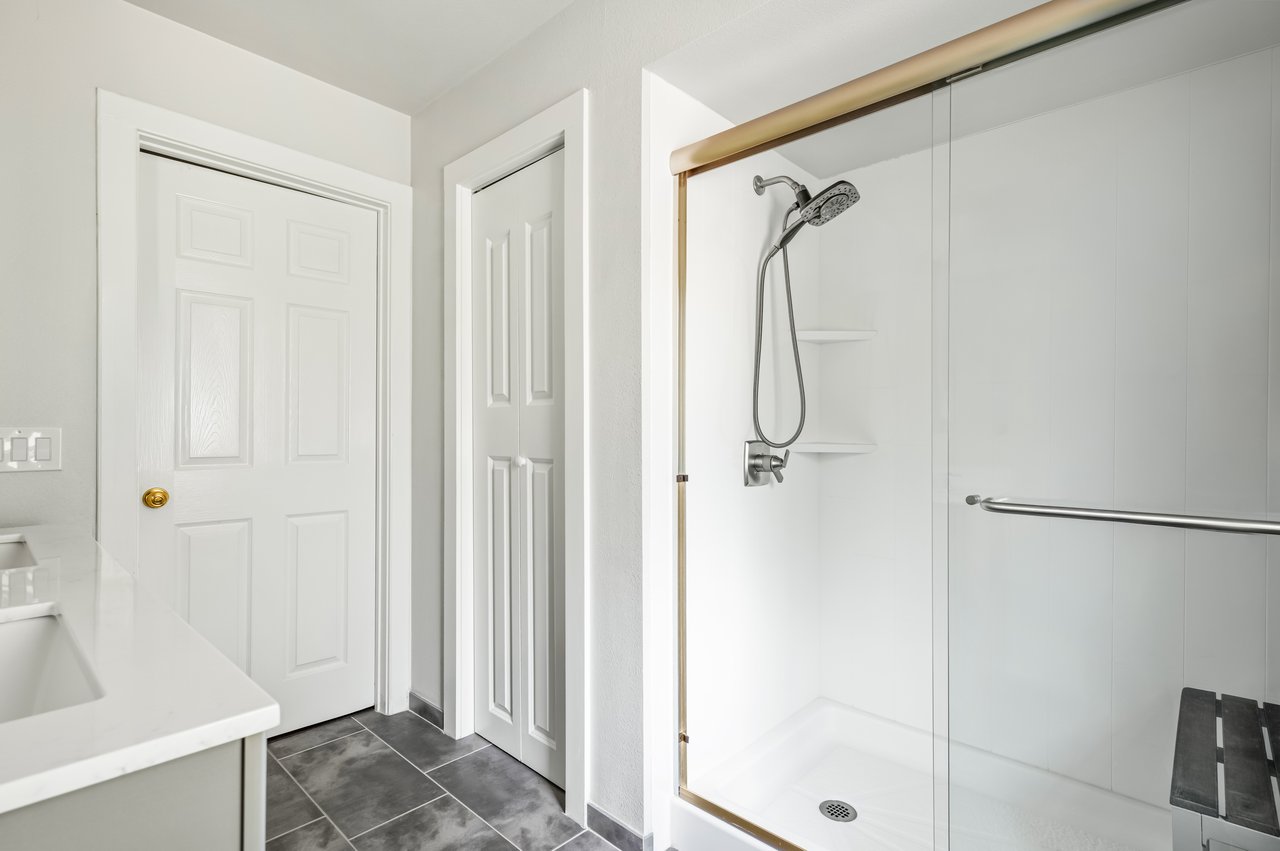 Bathroom with a glass walk-in shower, gold-tone trim, handheld showerhead, and dark tile floor.