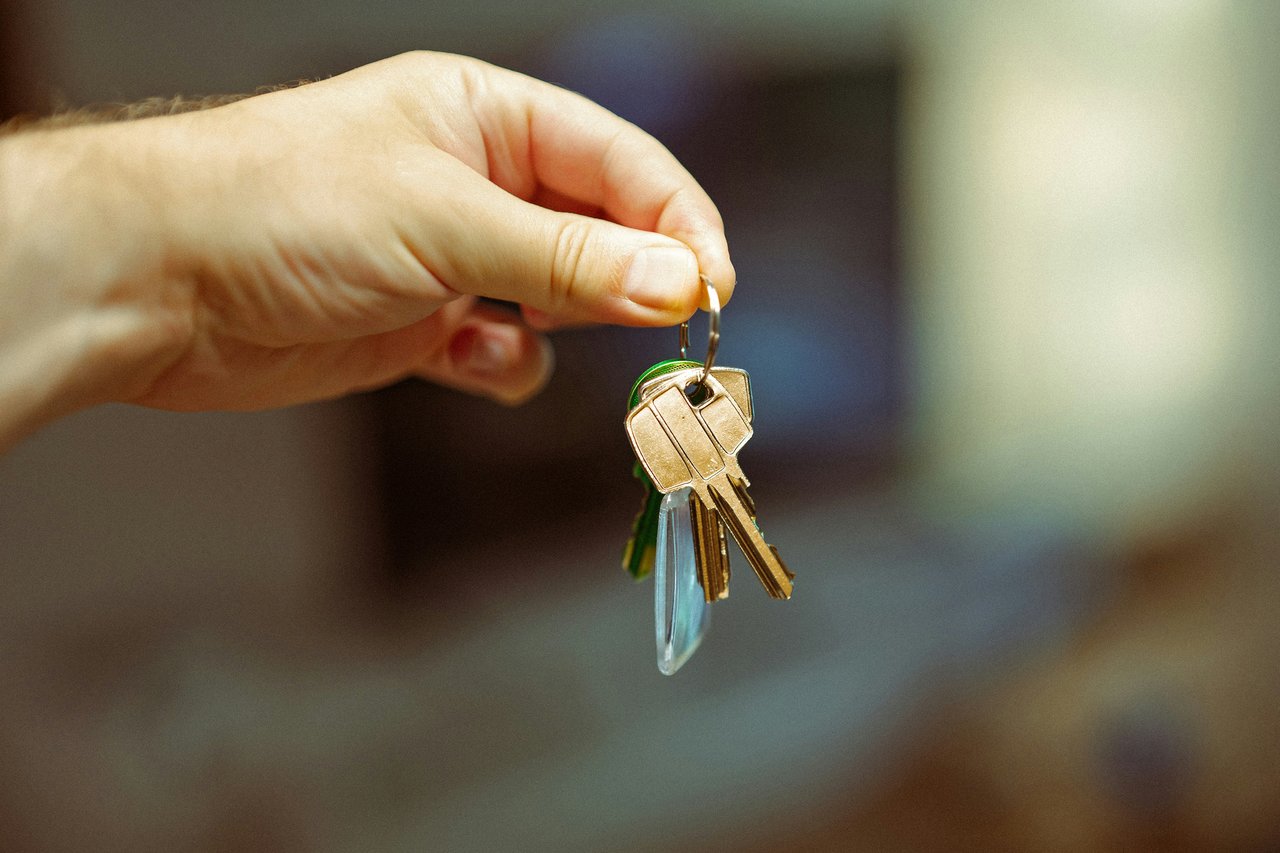 A hand holds several keys, including brass keys and a blue key fob.