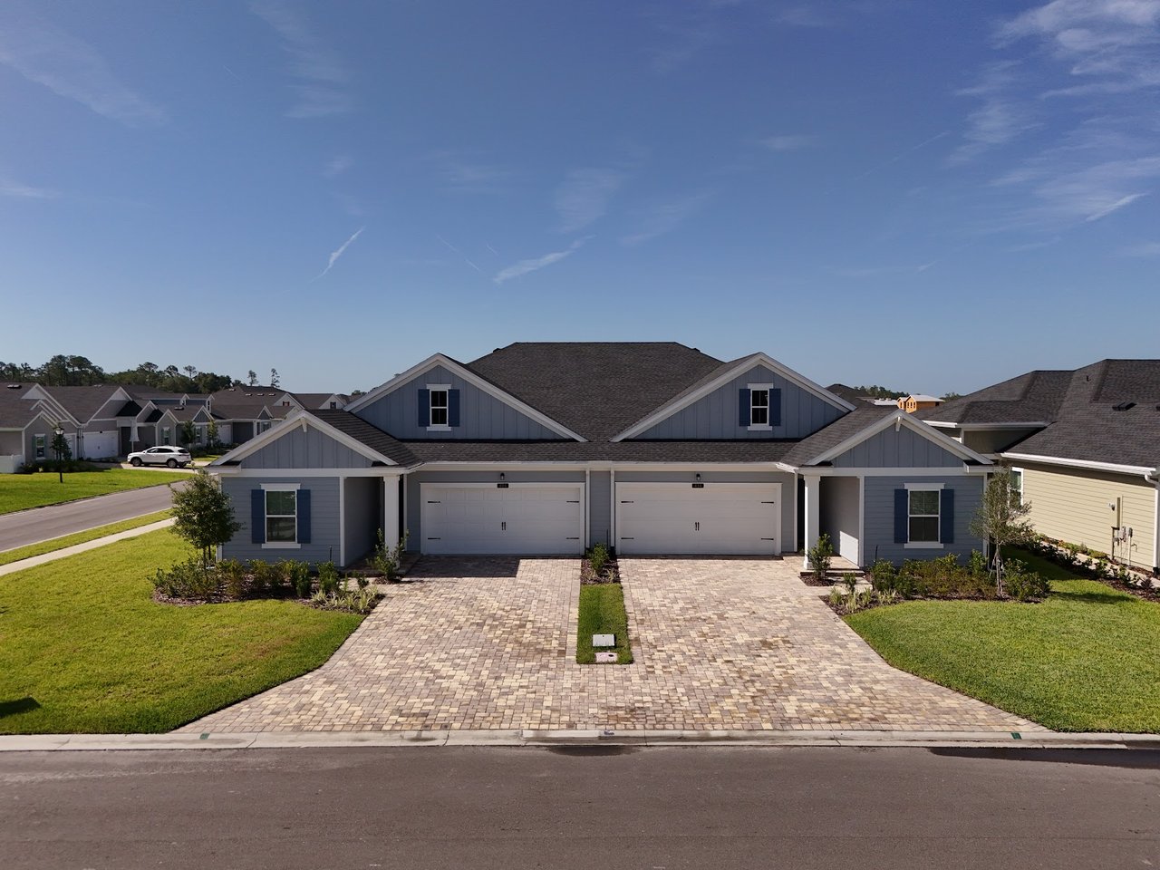 Attached blue-gray homes with white garage doors, broad paver driveways, and green lawns.
