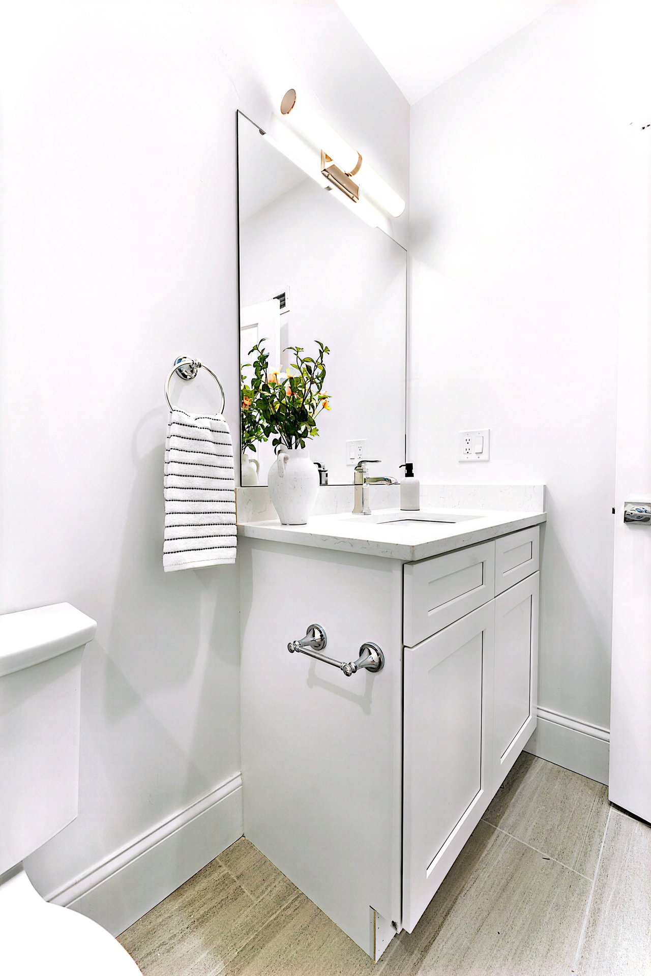 Bright bathroom with a white vanity, large mirror, chrome fixtures, and a striped hand towel.