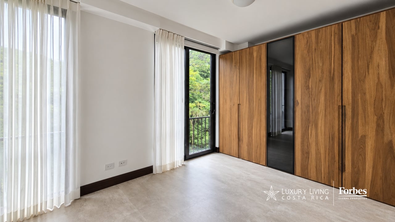 Empty bedroom with full-height wood wardrobes and a glass door opening to a leafy balcony.