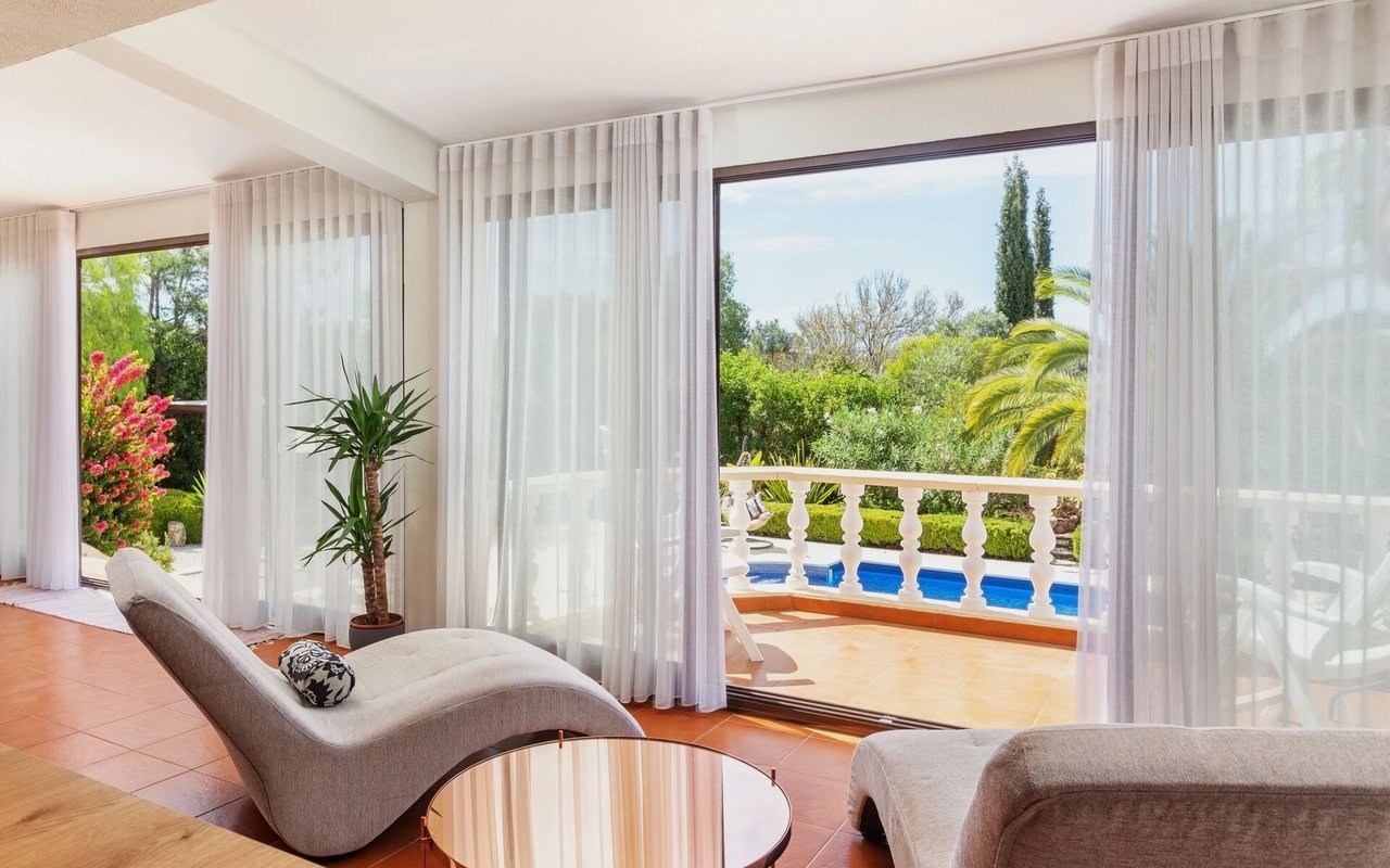 Living room with sheer curtains opening onto a terrace and garden pool.