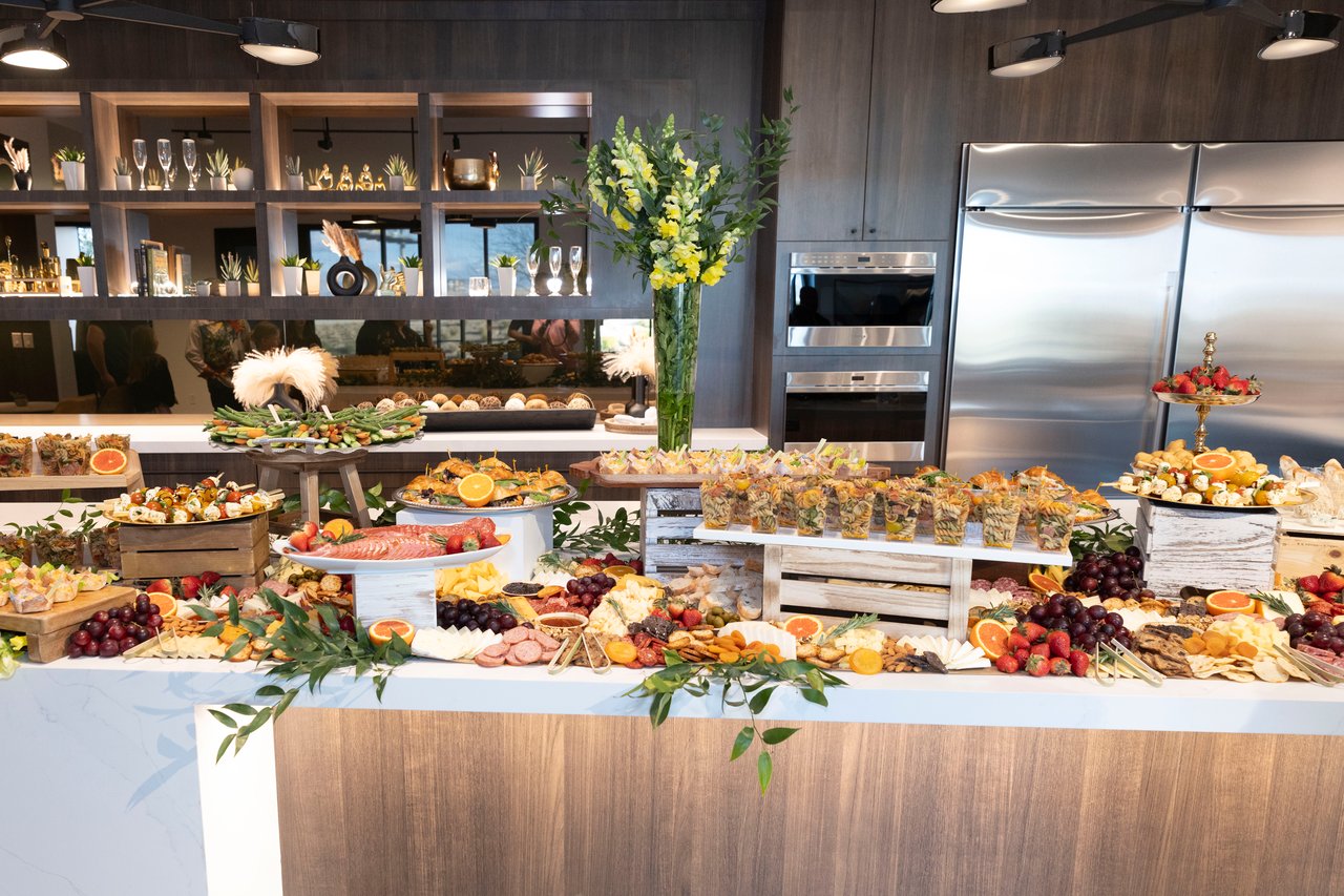 Open-house buffet with assorted appetizers, fruit, cheeses, and charcuterie on a kitchen island.