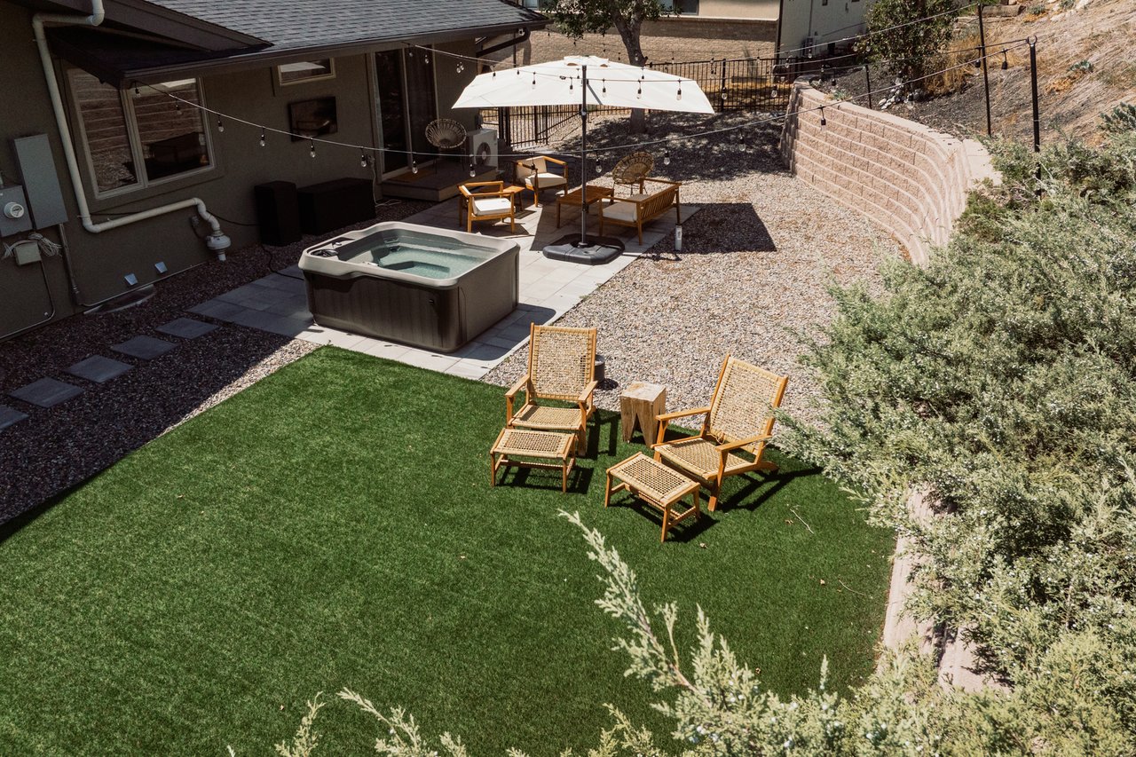 Backyard with a hot tub, umbrella-shaded patio seating, and artificial turf.