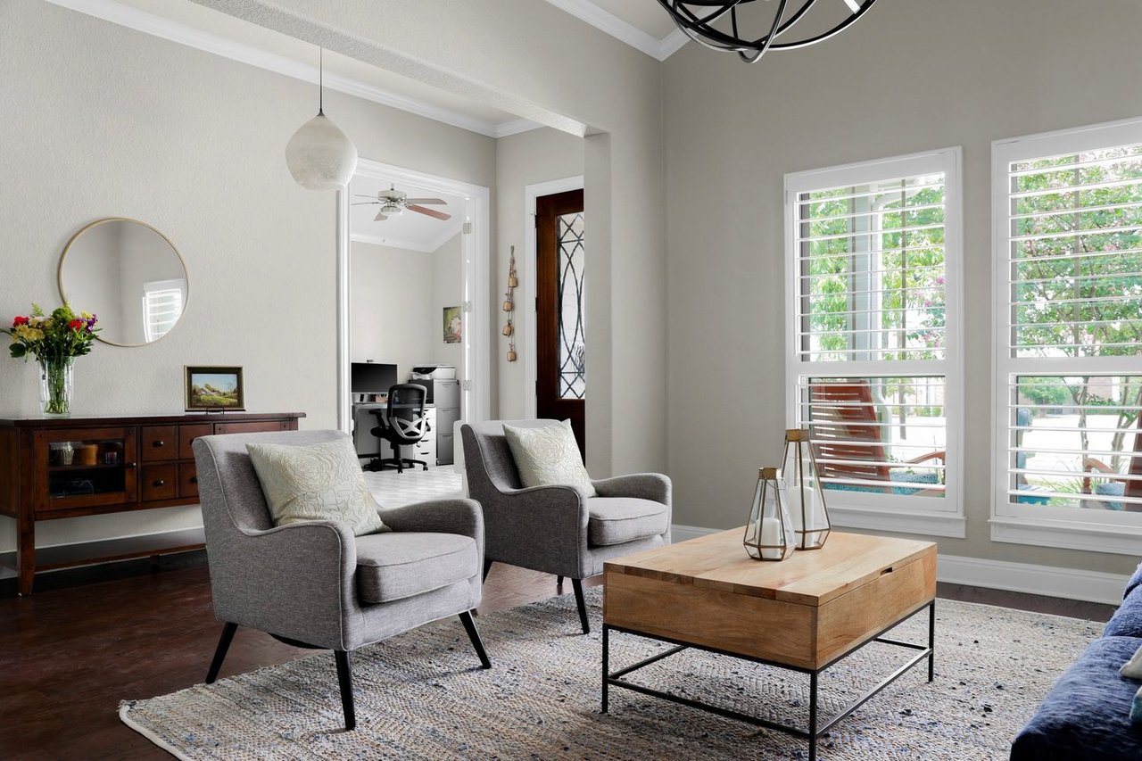 Living room with gray armchairs, a wood coffee table, and tall windows overlooking greenery.