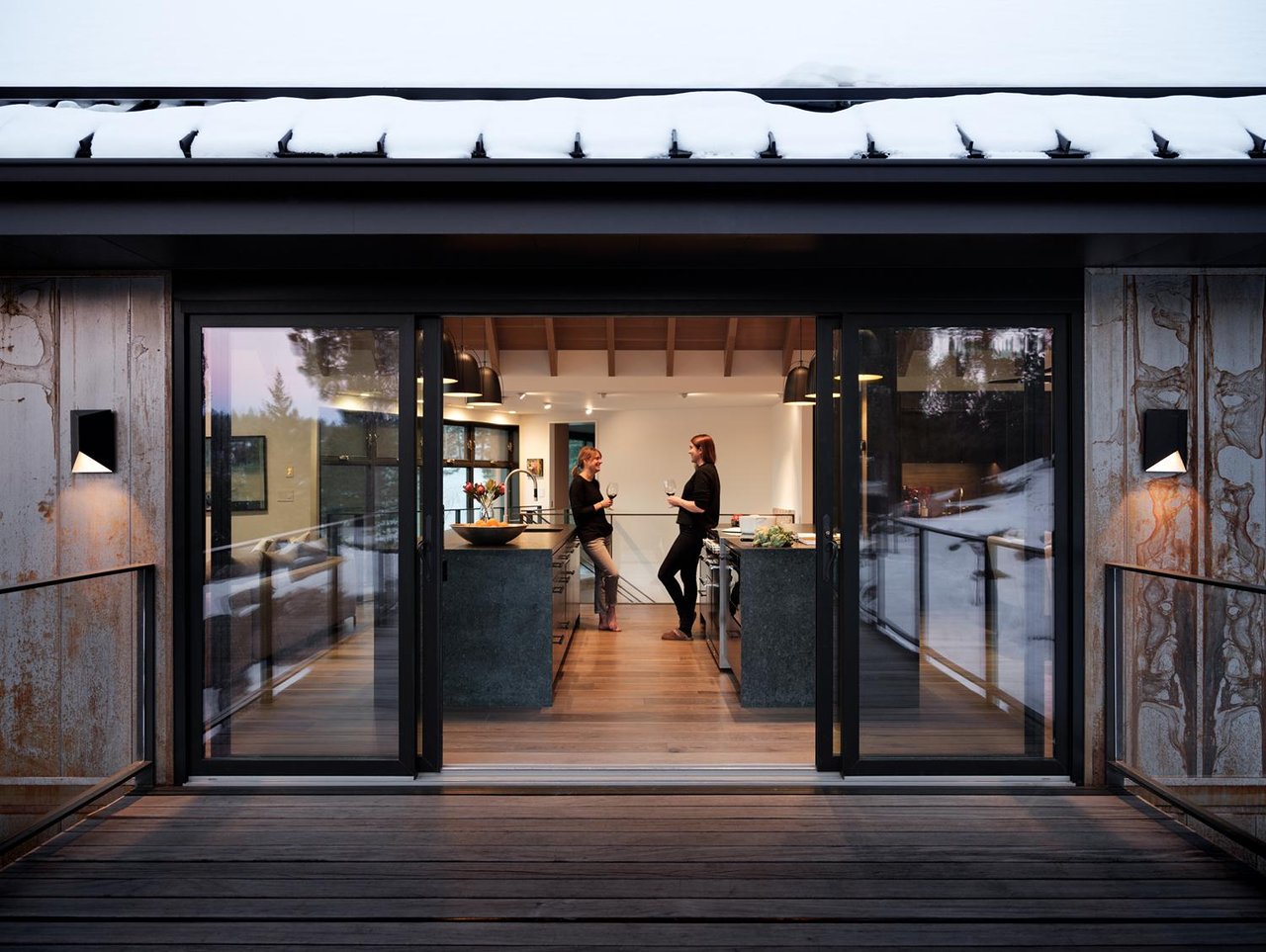 Boulder kitchen view through sliding glass doors with snow-covered roof, people conversing inside at dusk