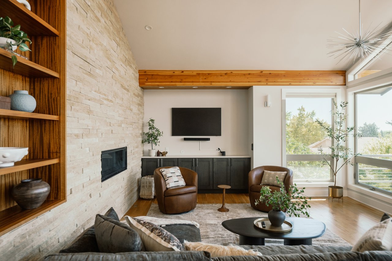 Living room with a pale stone fireplace wall, built-in wood shelves, leather chairs, and large windows.