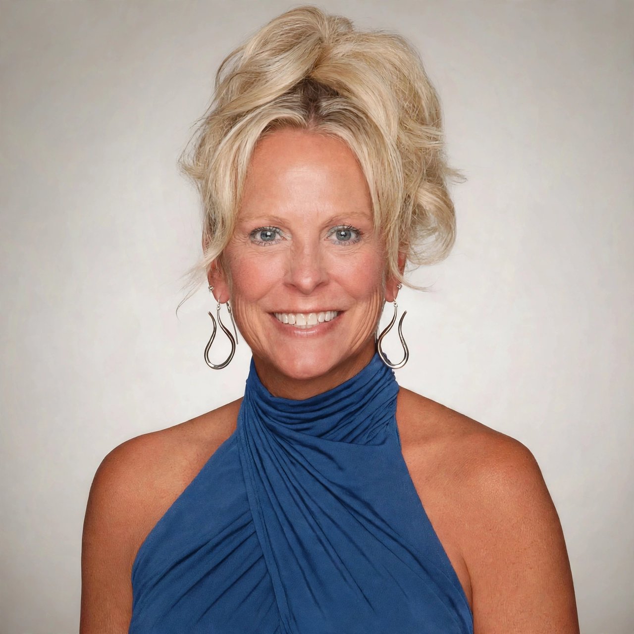 Carol York, smiling in a blue halter-style top and dangling earrings.