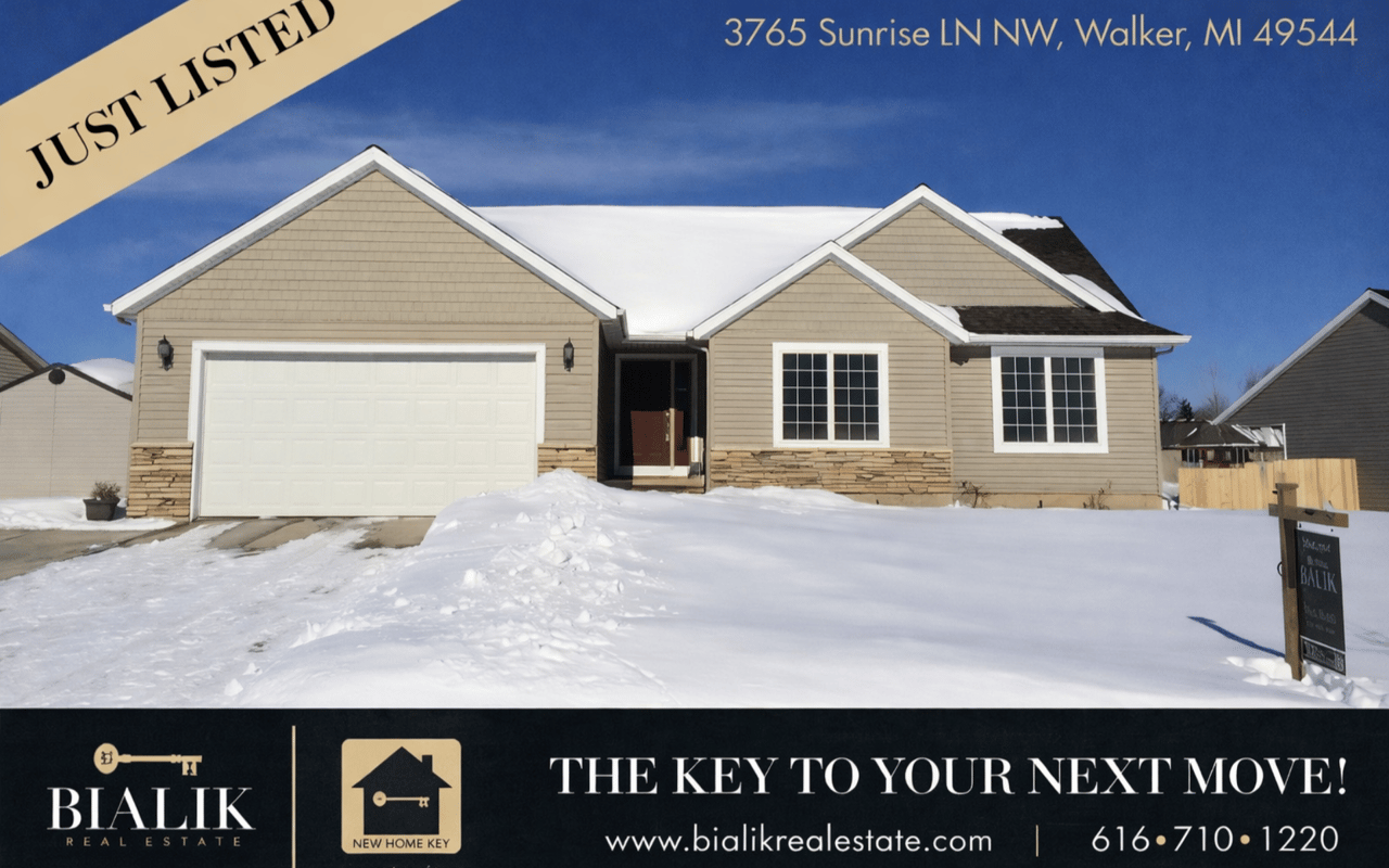 Beige single-story home with a two-car garage, stone accents, and a snow-covered yard.