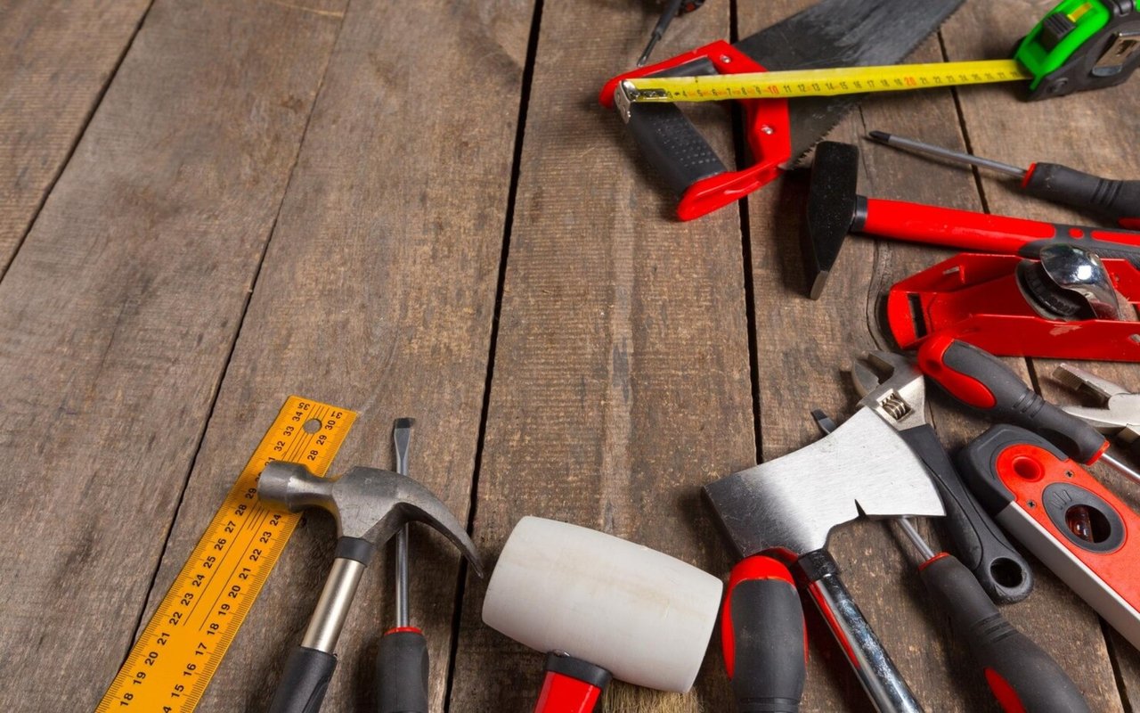 Home repair tools arranged on weathered wooden boards, including a tape measure, hammer, screwdrivers, and wrench.
