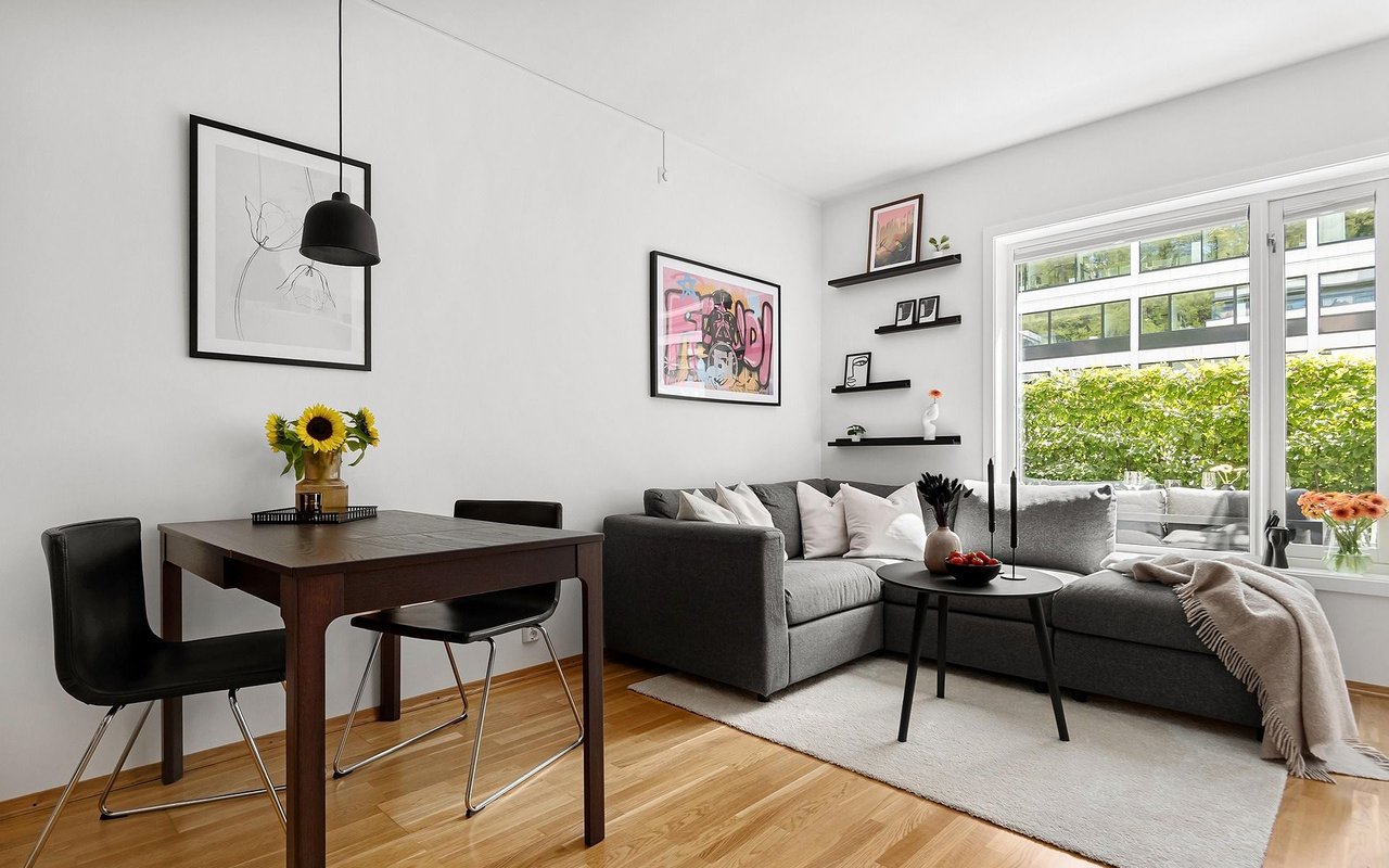 Living and dining area with a gray sectional, hardwood floors, and large windows.