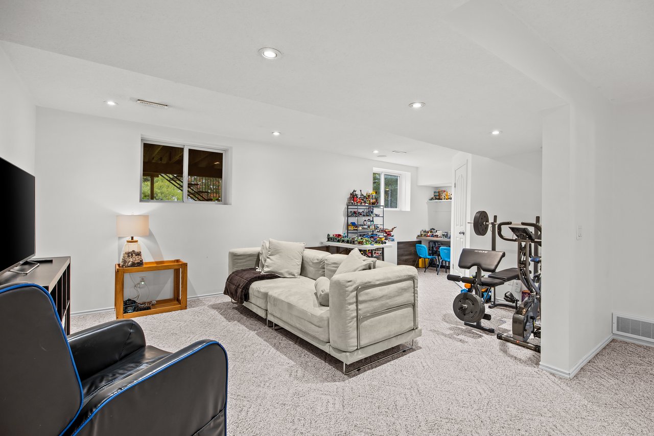 Basement recreation room with a sectional sofa, exercise equipment, and shelves of toys.
