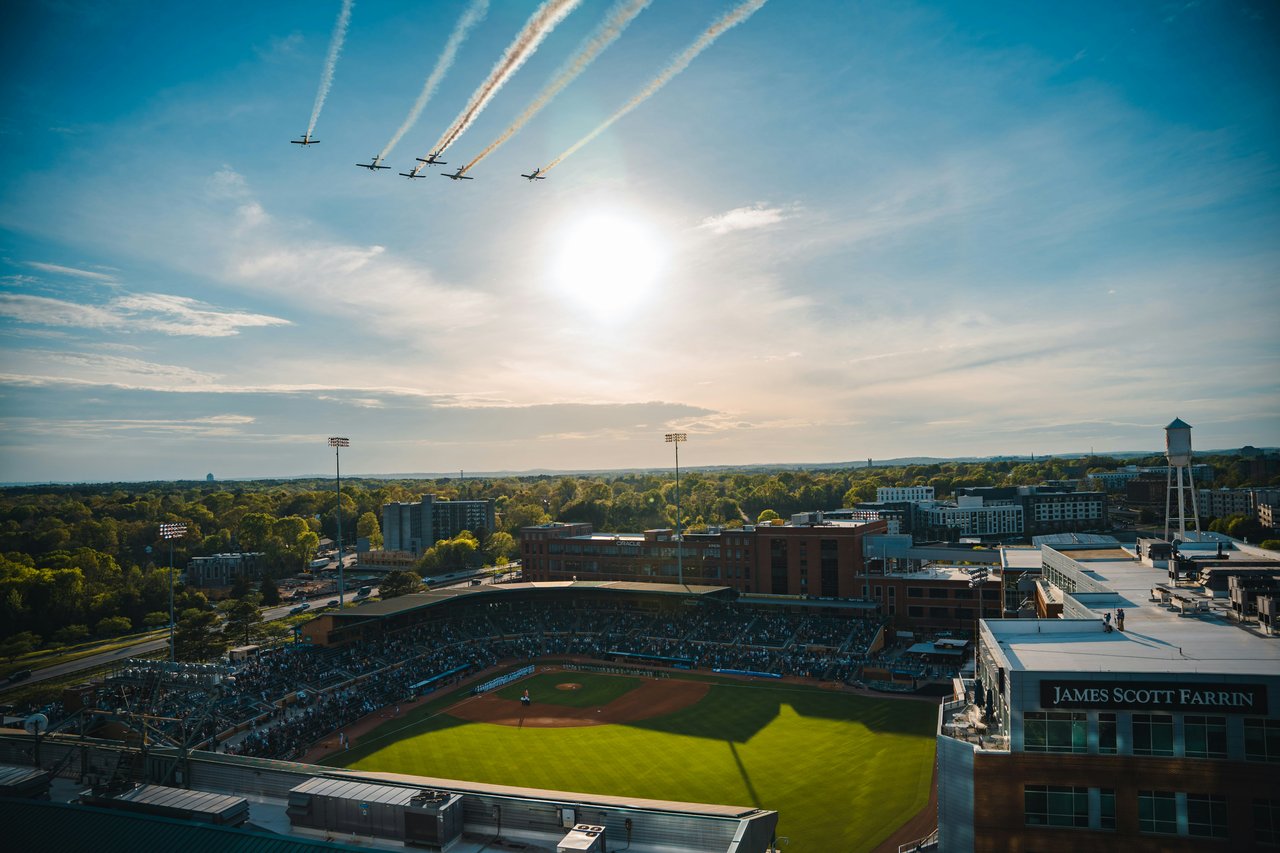 Baseball stadium during an aircraft flyover, with the sun low over the surrounding city.