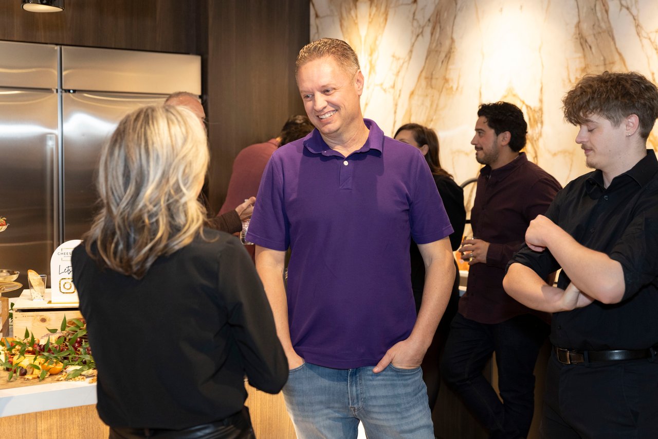 Guests mingle at an open house in a modern kitchen, with a food display beside them.