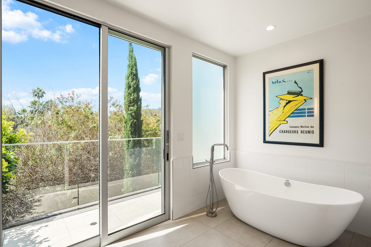 Modern bathroom with a freestanding tub beside glass doors opening onto a green terrace.