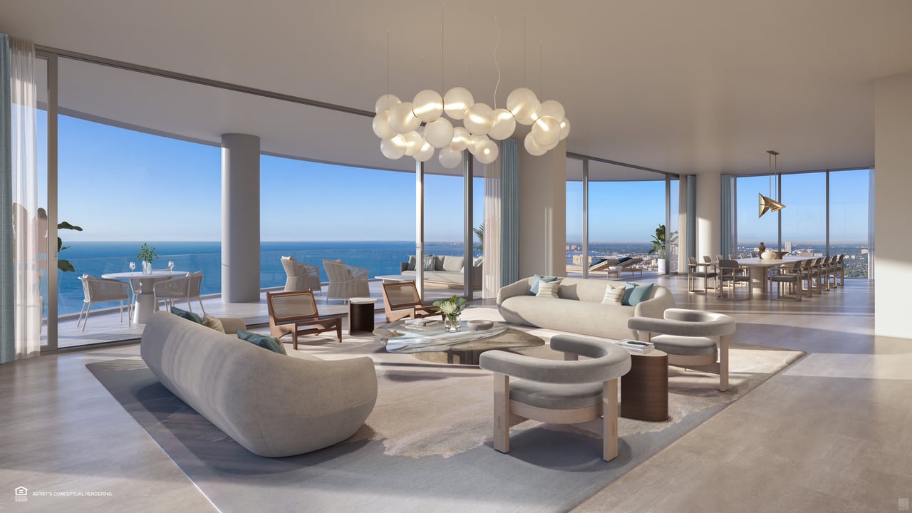 Furnished luxury living room with floor-to-ceiling windows overlooking the ocean and distant city skyline.