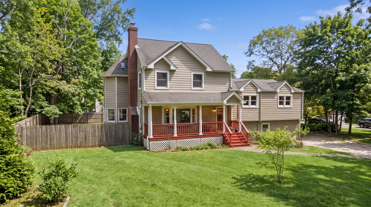 Two-story beige house with a red-railed porch, brick chimney, and broad green lawn.