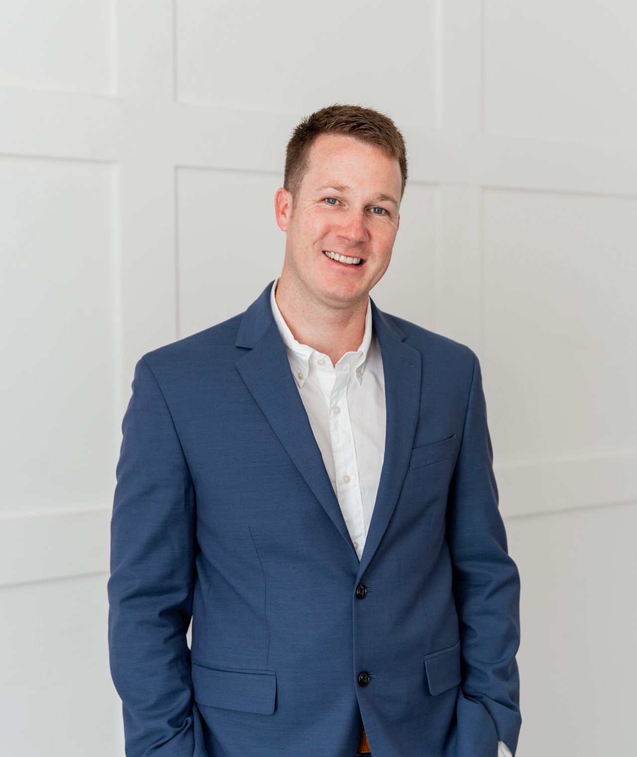 Kyle Taylor wearing a blue suit and white shirt against a white paneled wall.