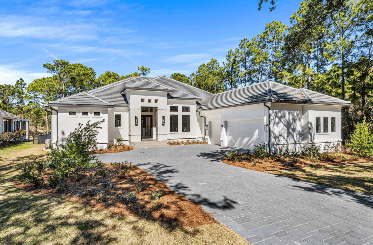 White single-story home with a gray tiled roof, covered entry, and broad paved driveway.