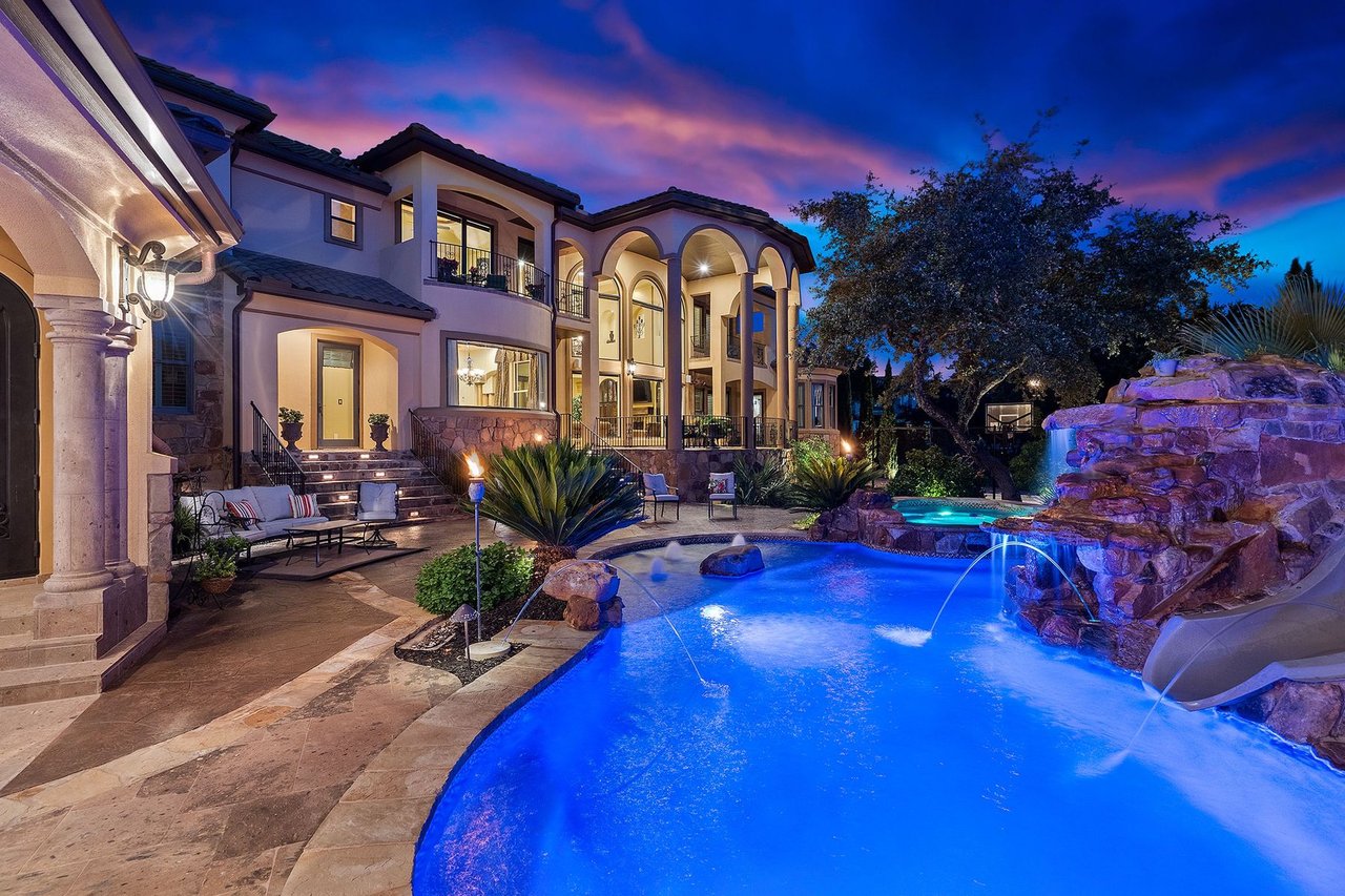 Twilight view of the pool with a stone grotto, waterfall, and slide at 25715 Cliff Circle, Lakecliff on Lake Travis, Spicewood, Texas.