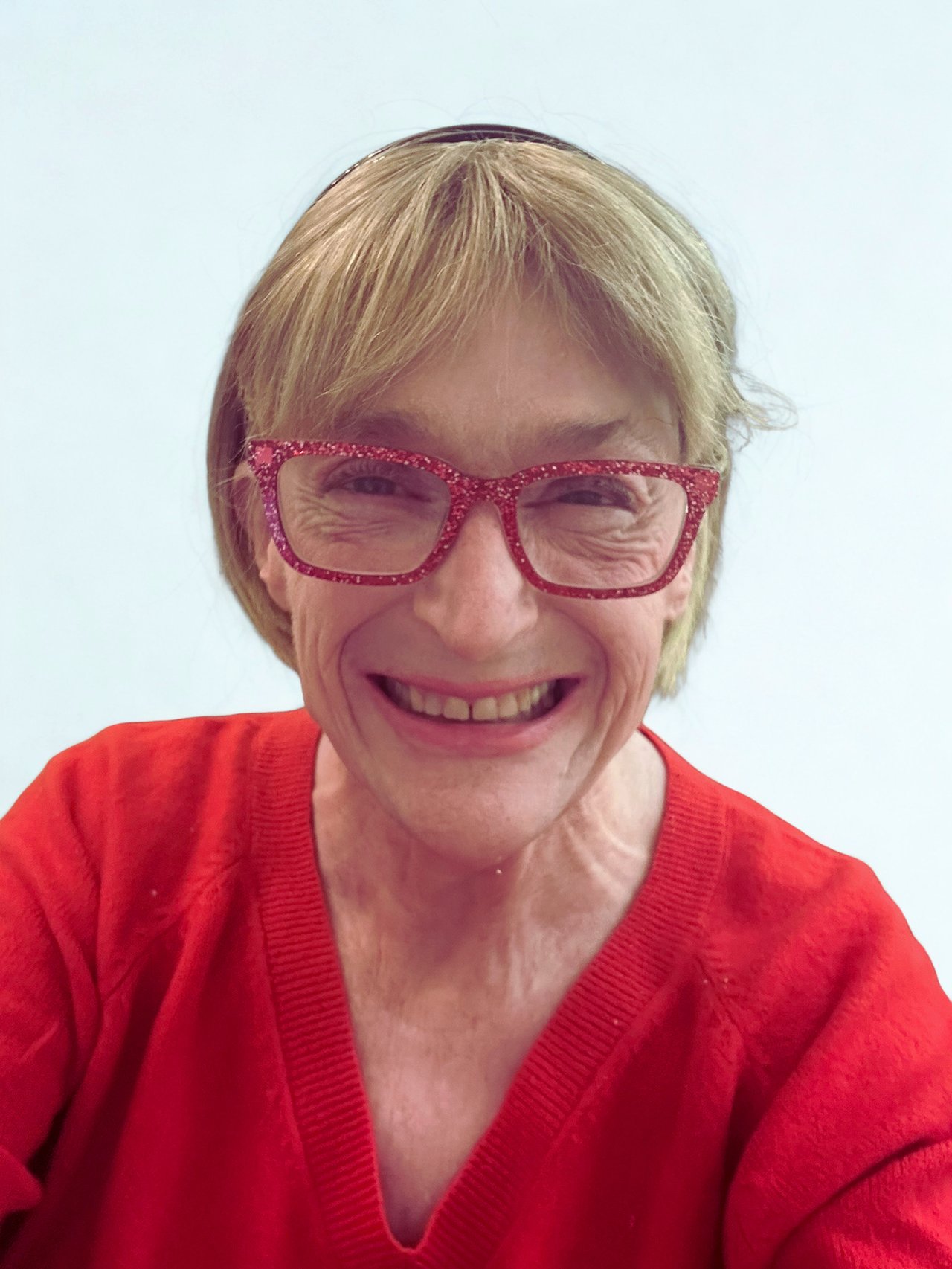 Sheryl Cleveland smiling in red glittery glasses and a red sweater.