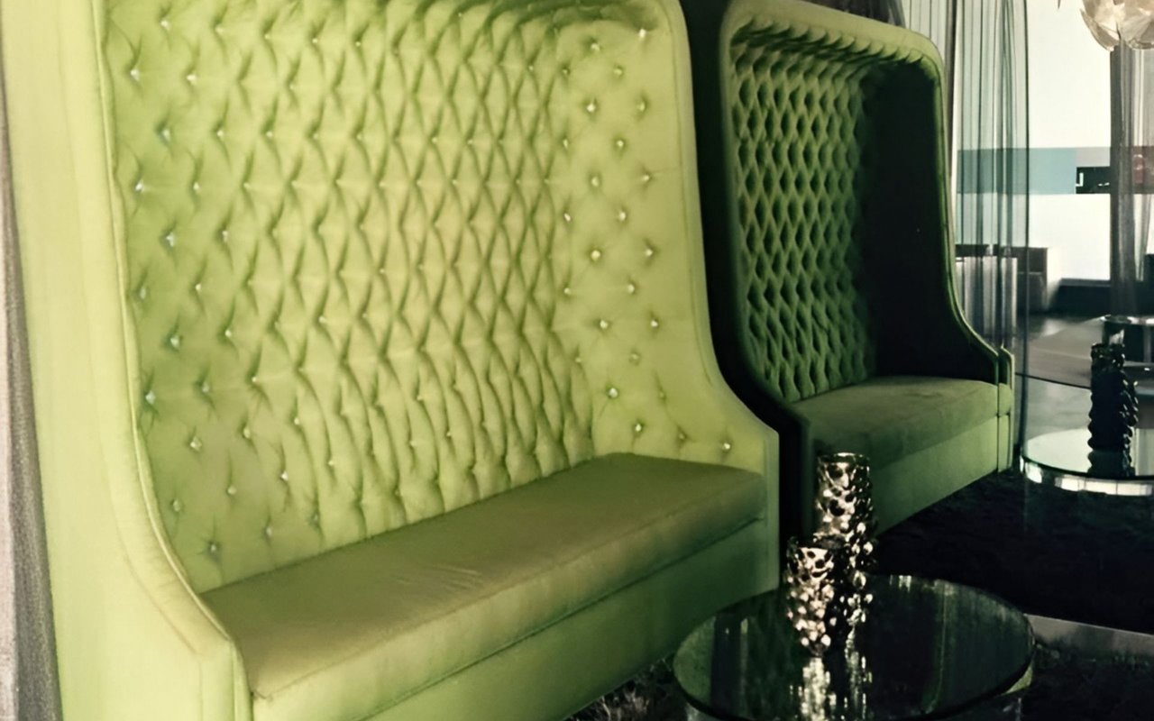 Lime-green tufted lounge chairs and reflective tables in a modern lobby.
