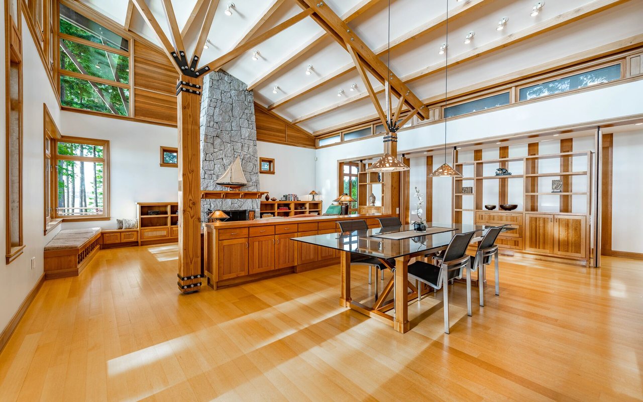 Open-plan dining room with exposed timber beams, a stone fireplace, and expansive windows.