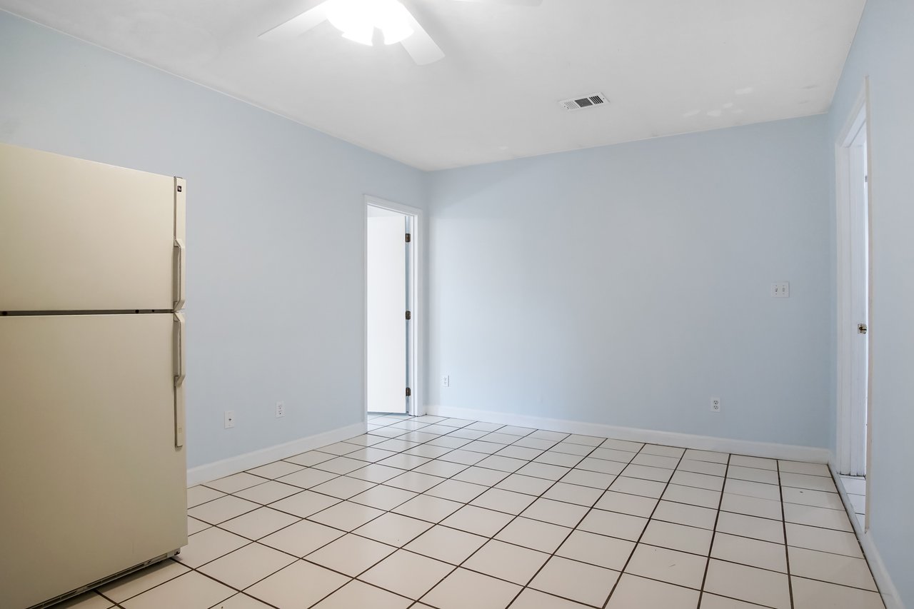 Empty room with light blue walls, white tiled floor, and a beige fridge on the left. Doorways lead to other rooms, conveying a sense of spaciousness.