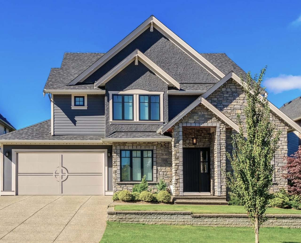 Two-story stone-and-siding home with a two-car garage, gabled roof, and landscaped lawn.