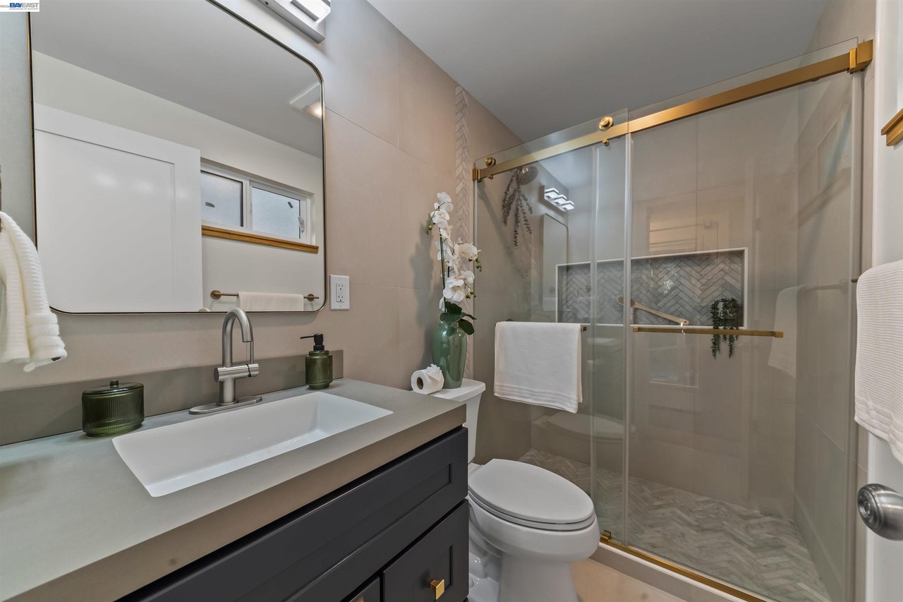 Bathroom with a dark vanity, white sink, and glass shower with brass hardware.