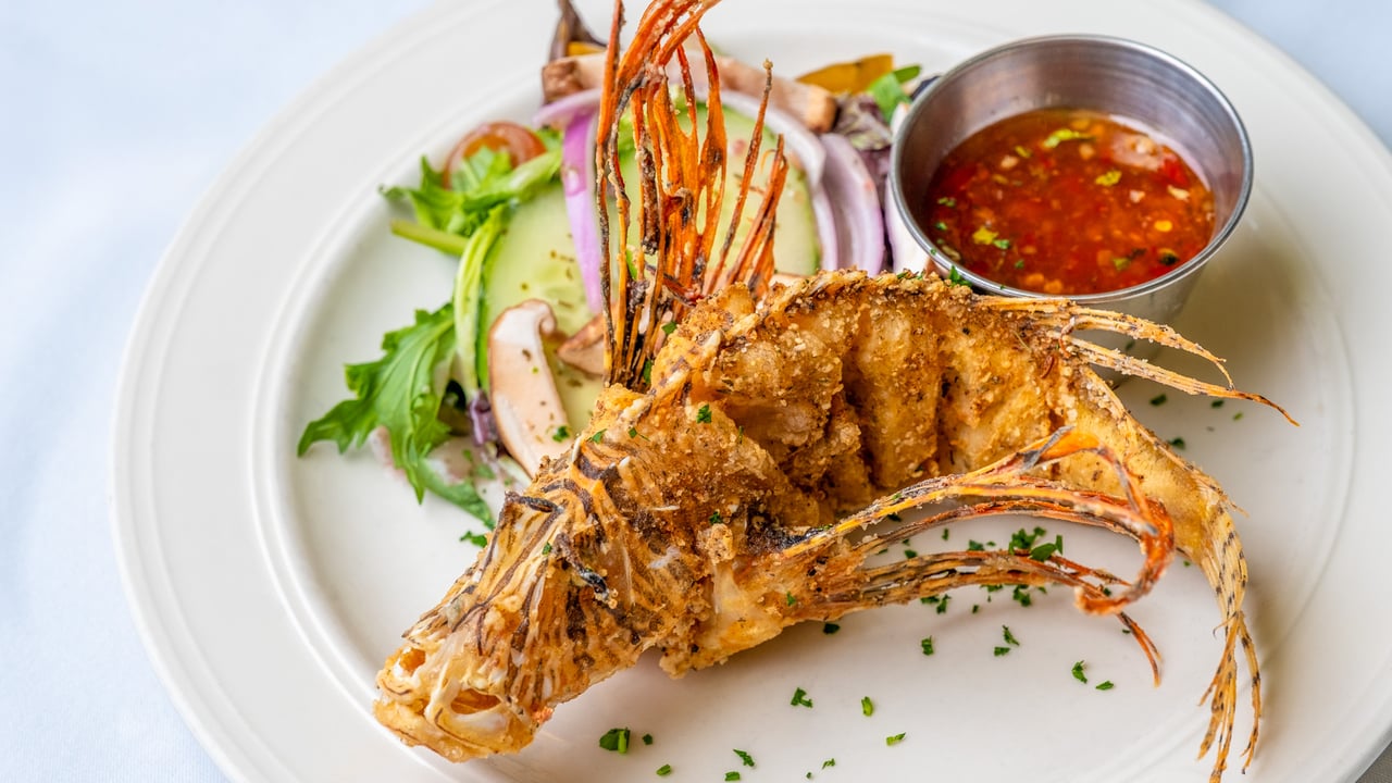 Golden fried whole fish with salad and a bowl of dipping sauce.