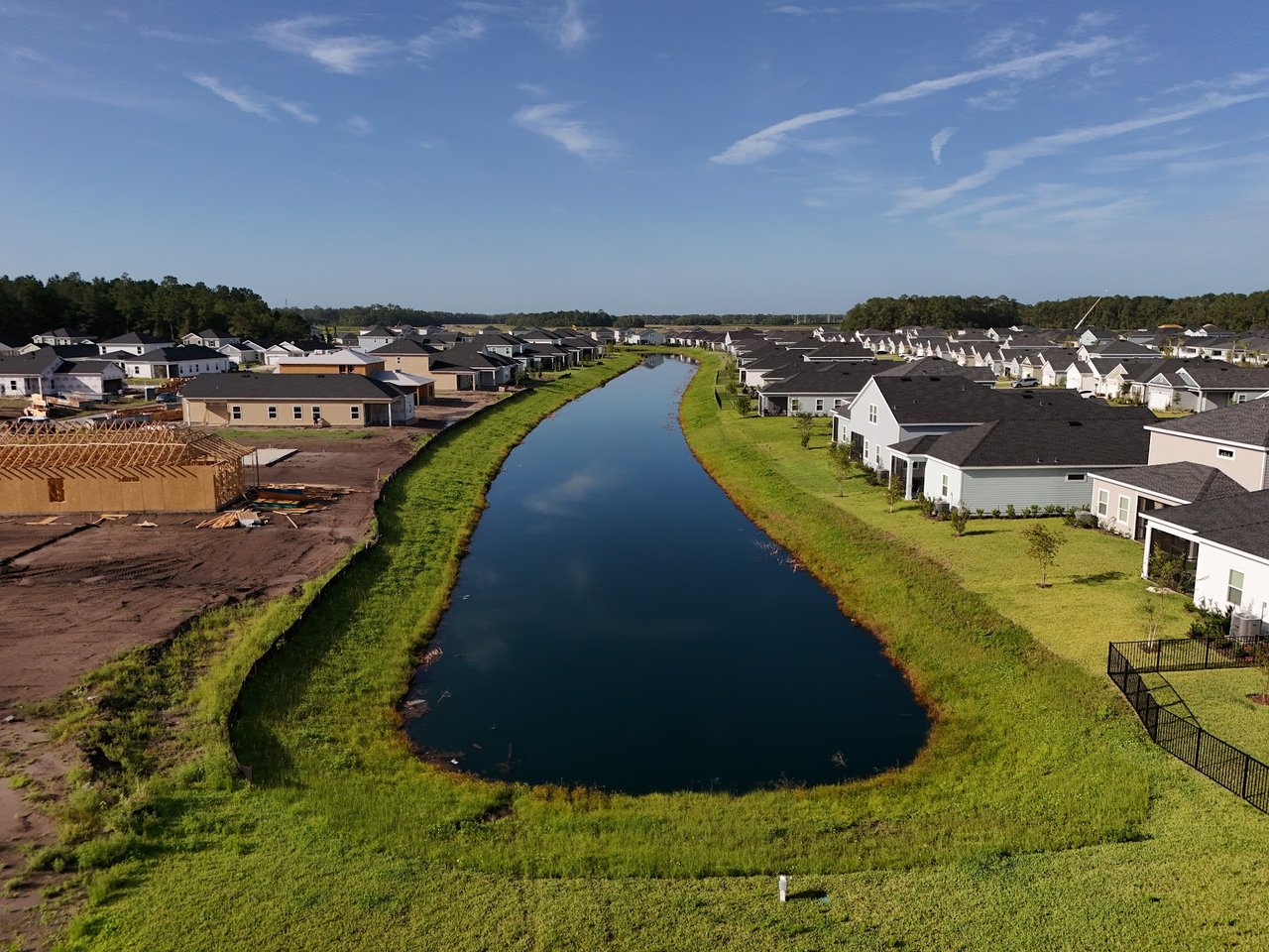 Aerial view of homes along a waterway, with an active construction site on the left bank.