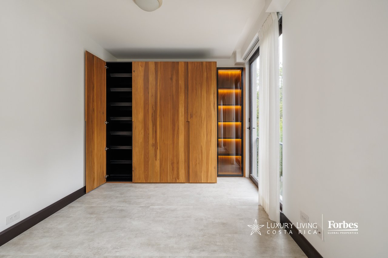 Vacant room with a large wood wardrobe, illuminated display shelves, and tall curtained windows.