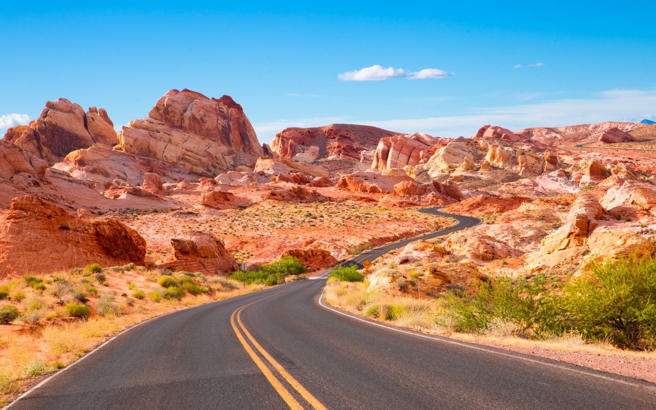 A winding road passes through red sandstone formations and sparse desert vegetation.