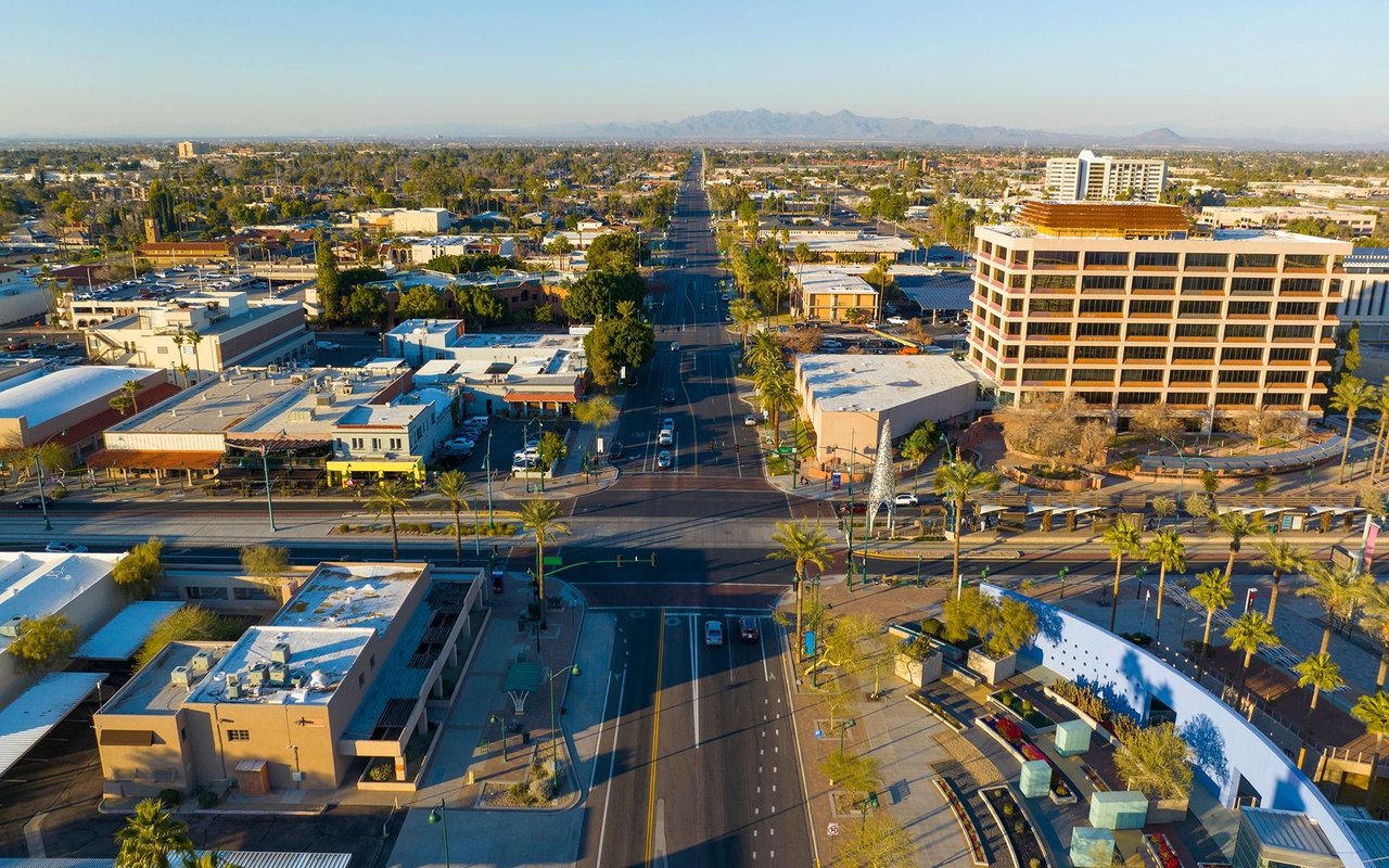Aerial view of a palm-lined Arizona city street with distant mountains and a large office building.