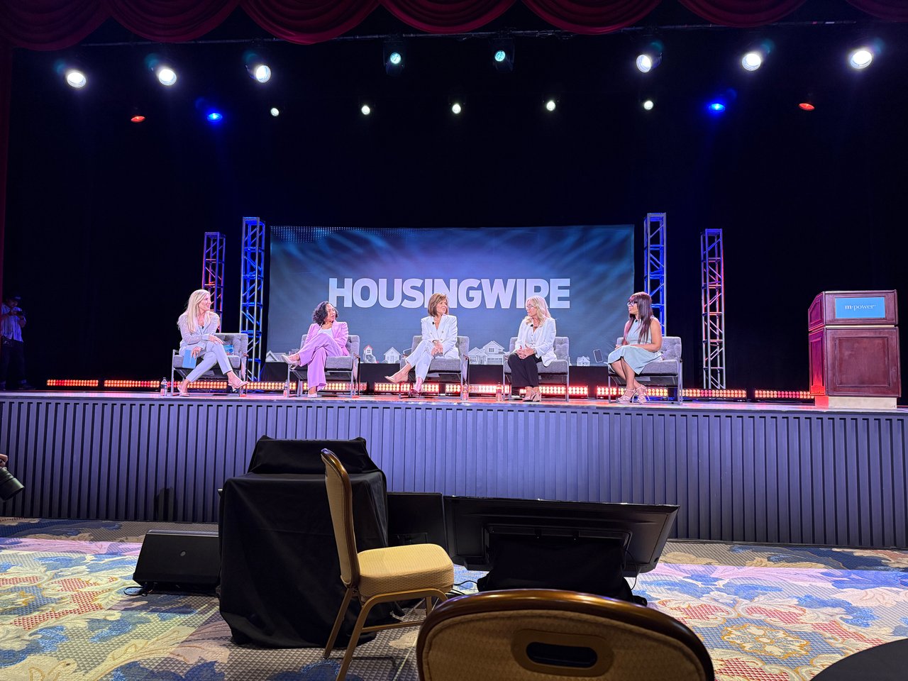 Five women sit onstage for a HousingWire panel beneath a large event backdrop.