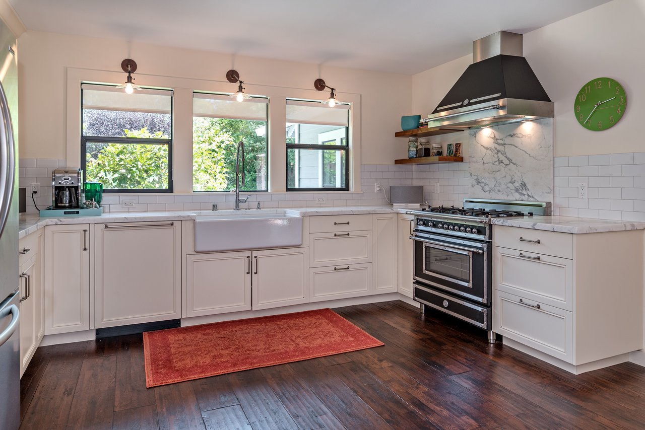 Bright white kitchen with a farmhouse sink beneath three windows and a stainless steel range.