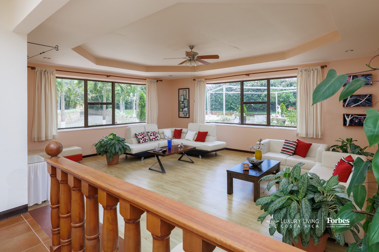 Furnished living room with white sectional sofas and large corner windows overlooking a garden.